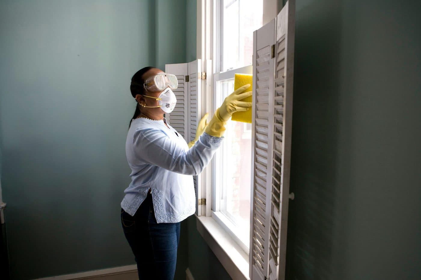 A person in gloves wiping a window frame
