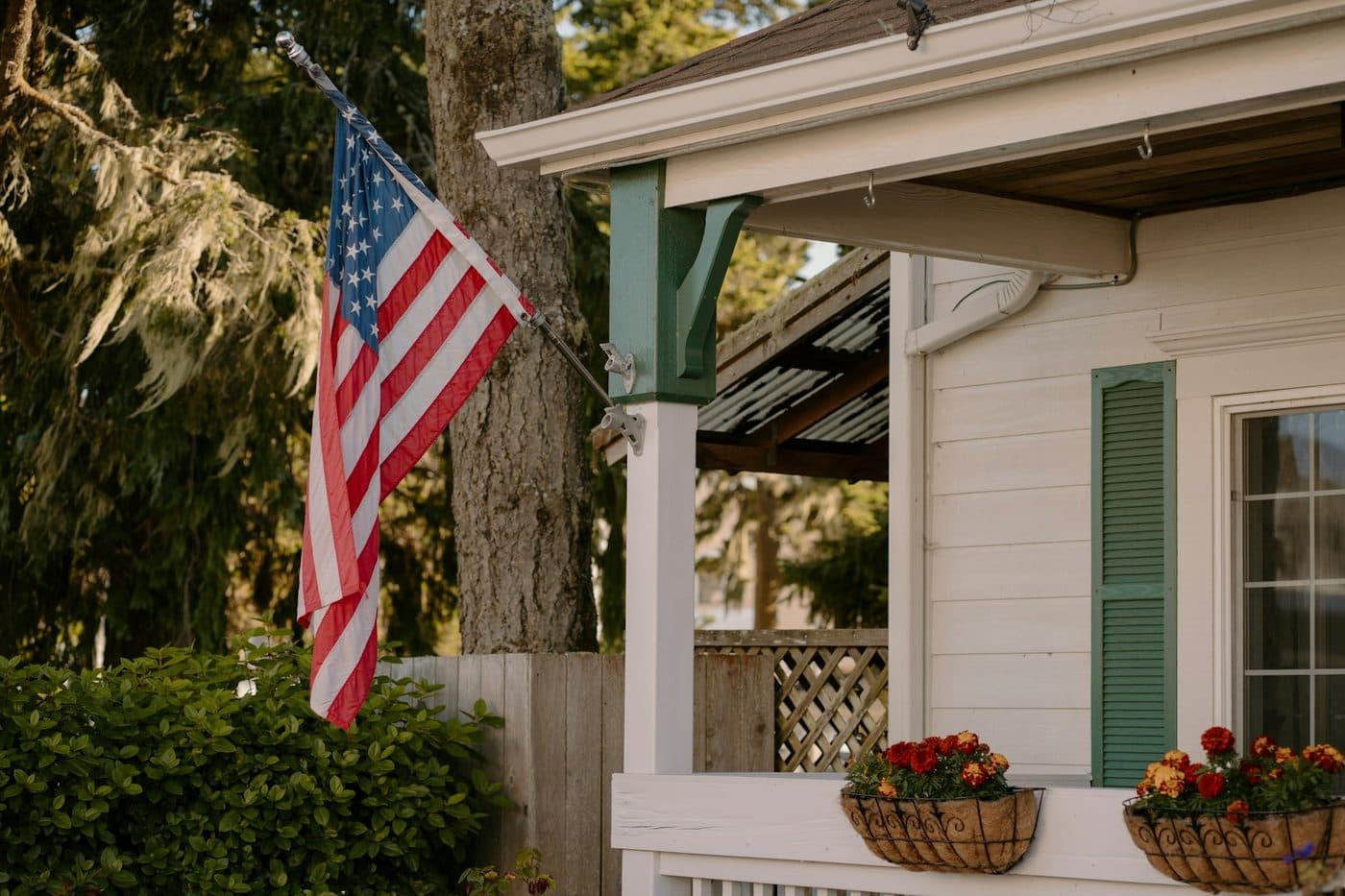 An American flag on a white house porch with green shutters