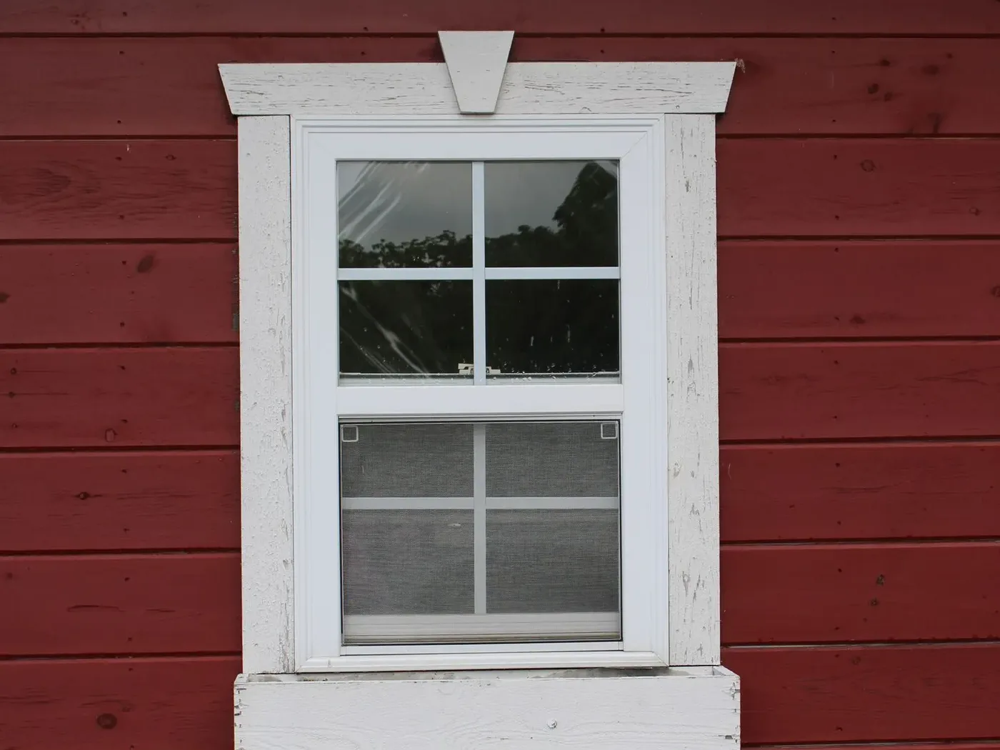 A white window surrounded by flat white trim on a red wall