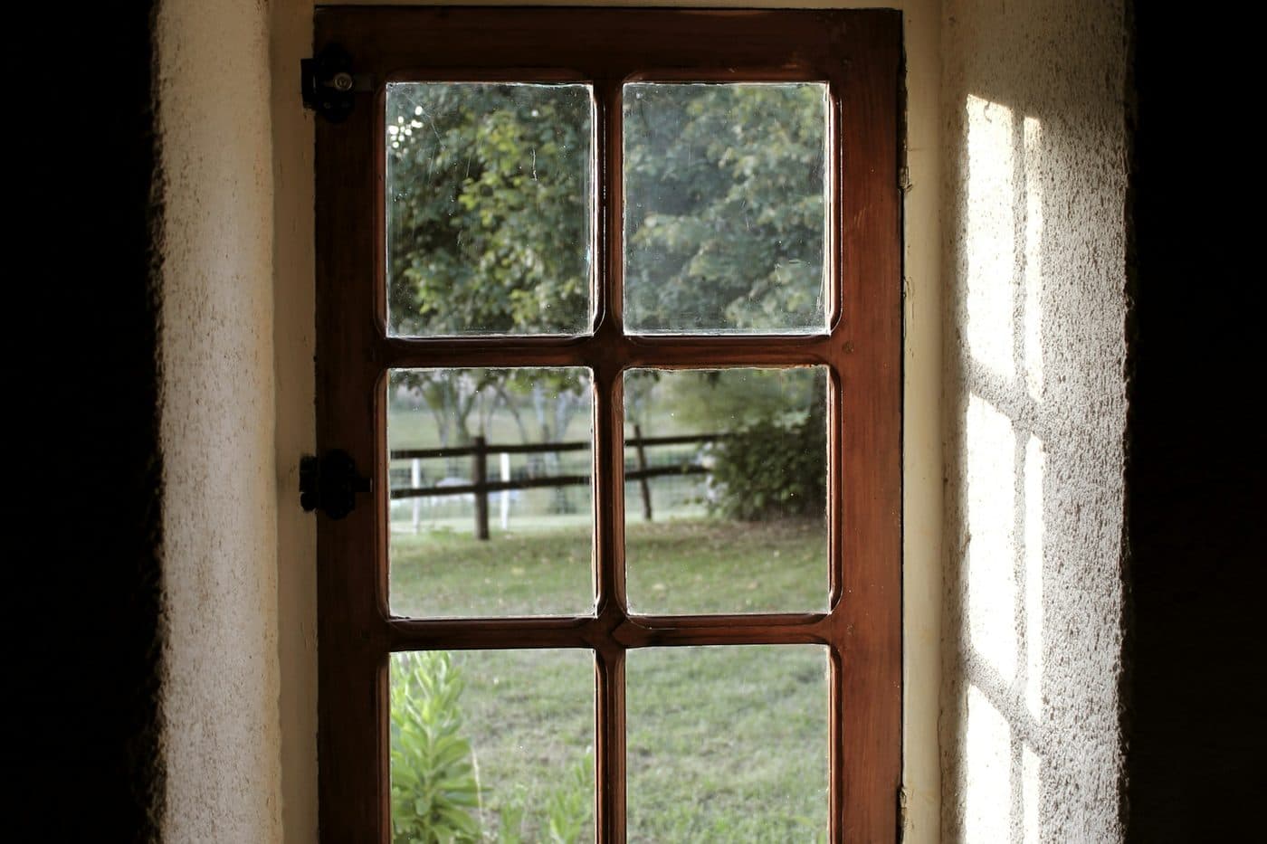 A small window with a wooden frame looking onto a garden